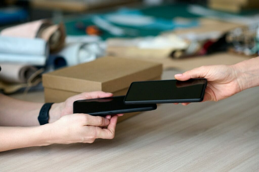 Close-up of hand of buyer holding smartphone over that of shop assistant