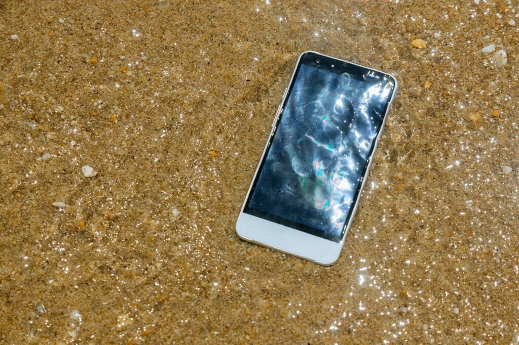 Broken crashed smartphone is lying in the water in the sandy beach